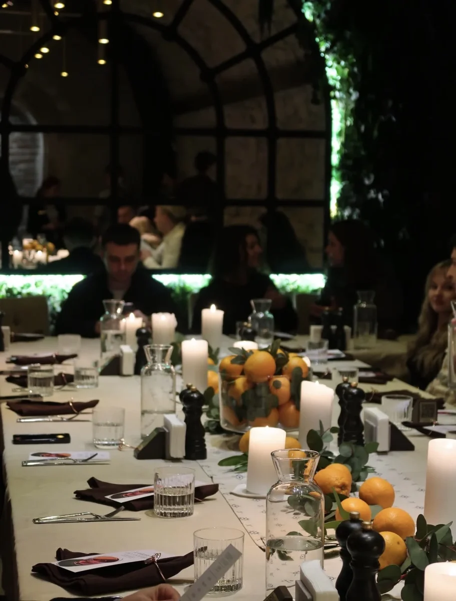 A festive table in a vaulted hall with candles and water carafes among greenery