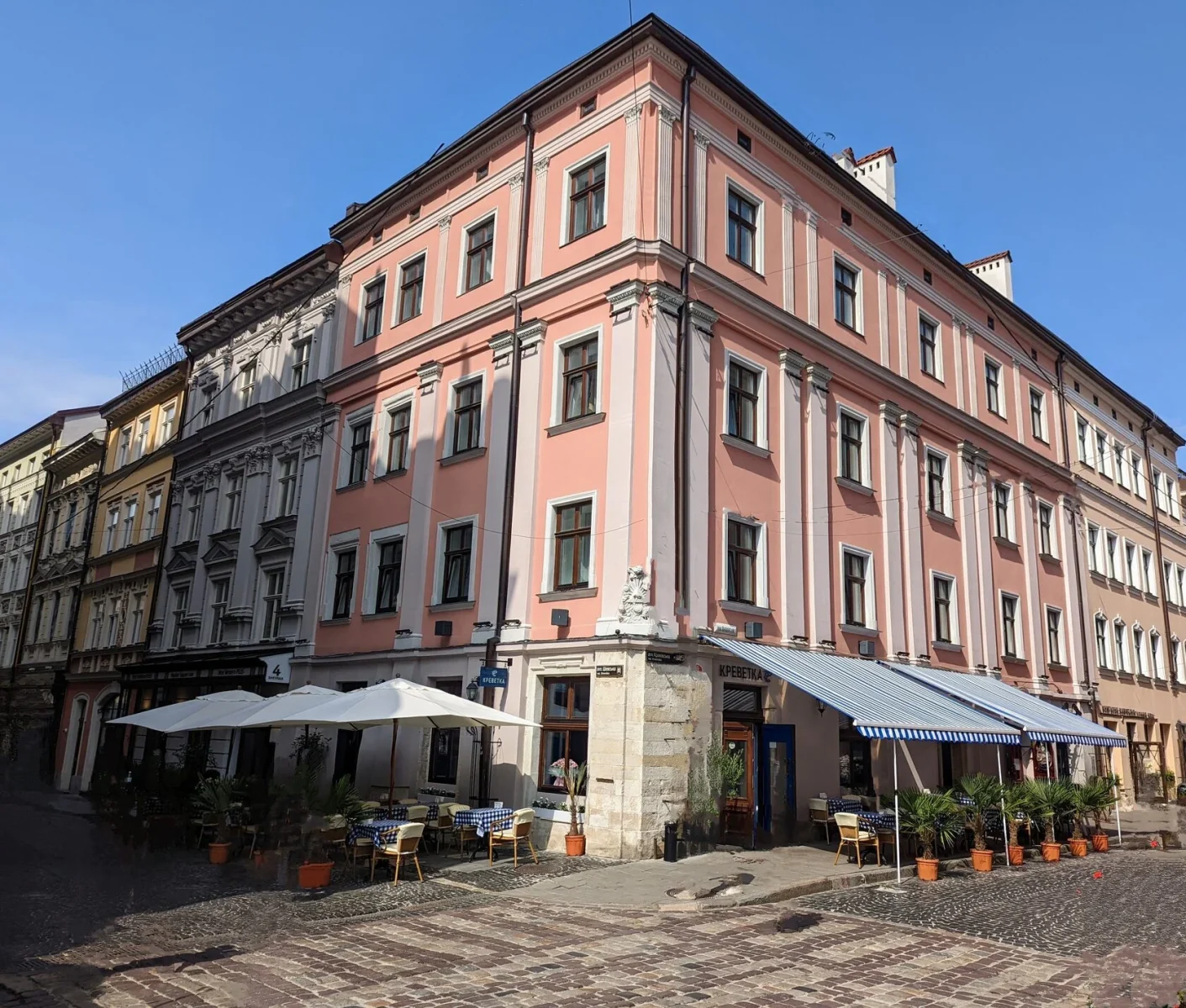 A pink corner building with white pilasters and a summer cafe terrace