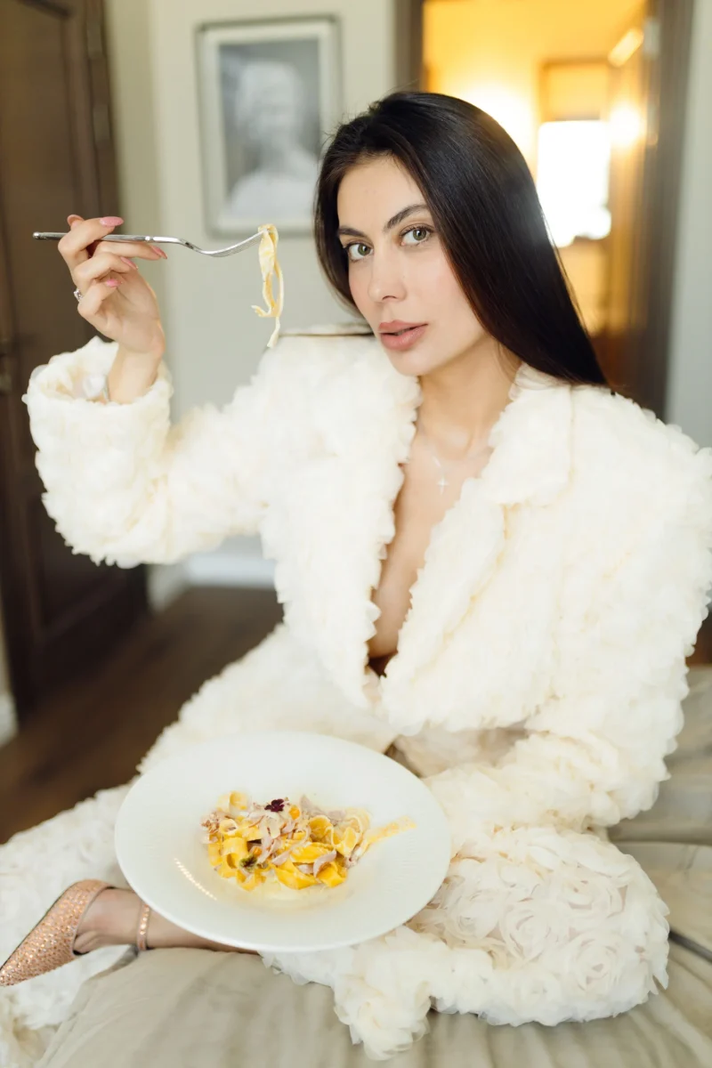 A guest in a white jacket having pasta on the bed