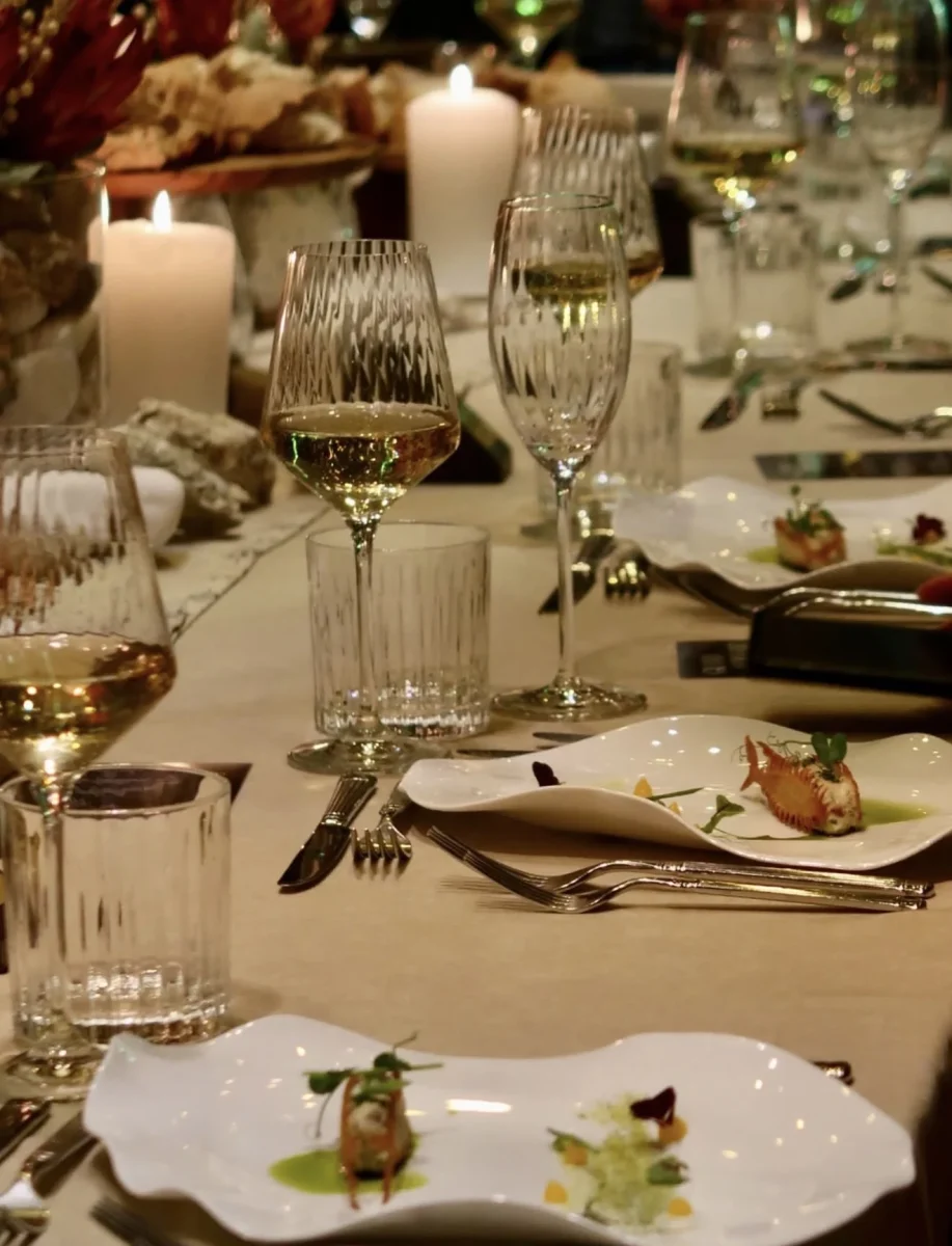 Glasses of white wine and candles above scalloped plates with a fish starter